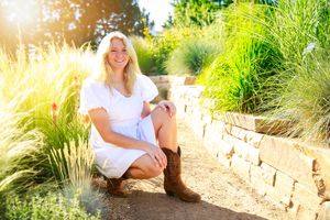 Someone in a white dress posing by ornamental grasses and a rock wall during golden hour sunlight.