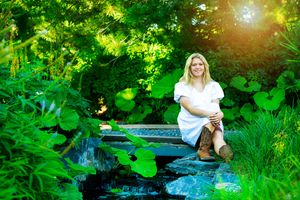 A serene creek flows through lush green foliage on a sunny summer day as sunlight streams through the trees.