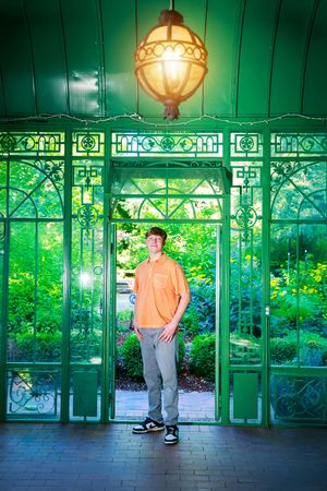 A person stands in an ornate green conservatory with decorative ironwork and glowing vintage lanterns casting a warm glow.