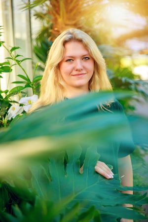 Portrait in a lush tropical garden setting with green foliage and soft sunlight filtering through the leaves.