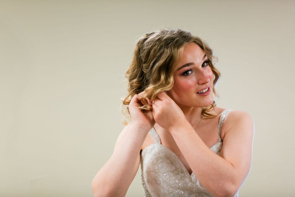Elegant bride in white dress putting on earrings while getting ready.