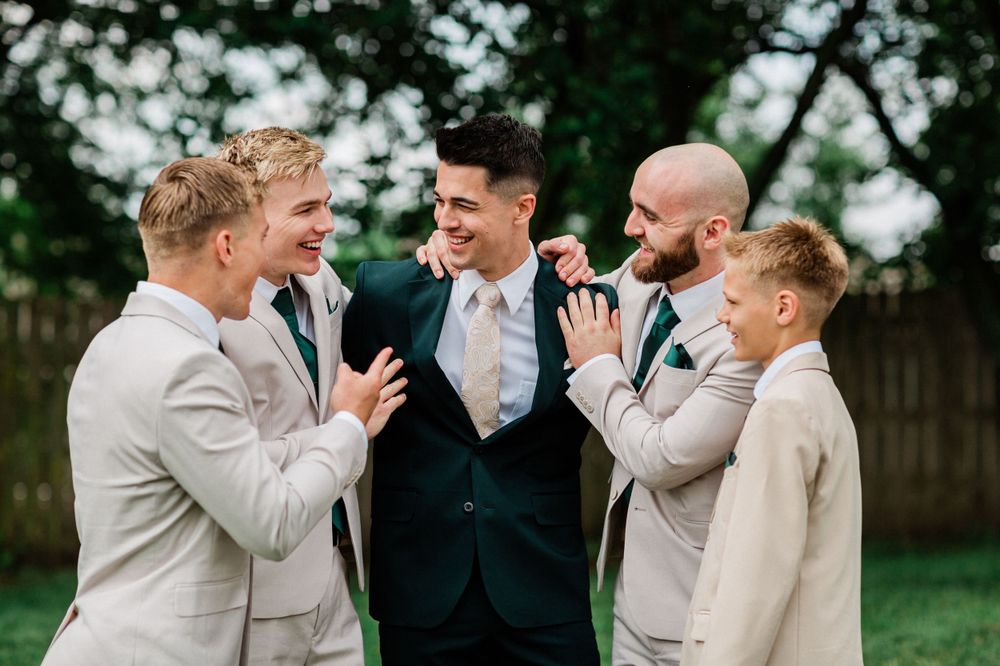 Groomsmen in light suits share a candid laughing moment with the groom.