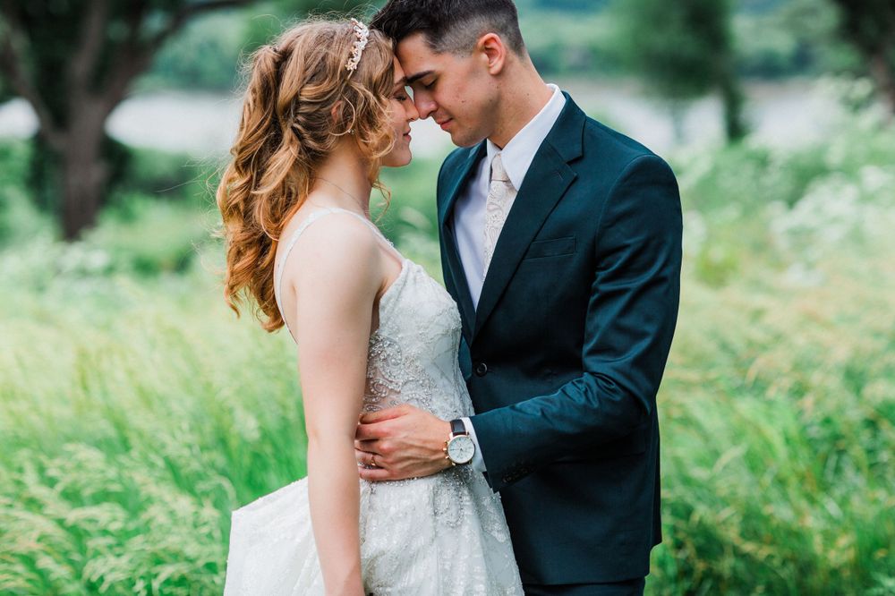 Intimate wedding portrait of couple in formal attire among green foliage.