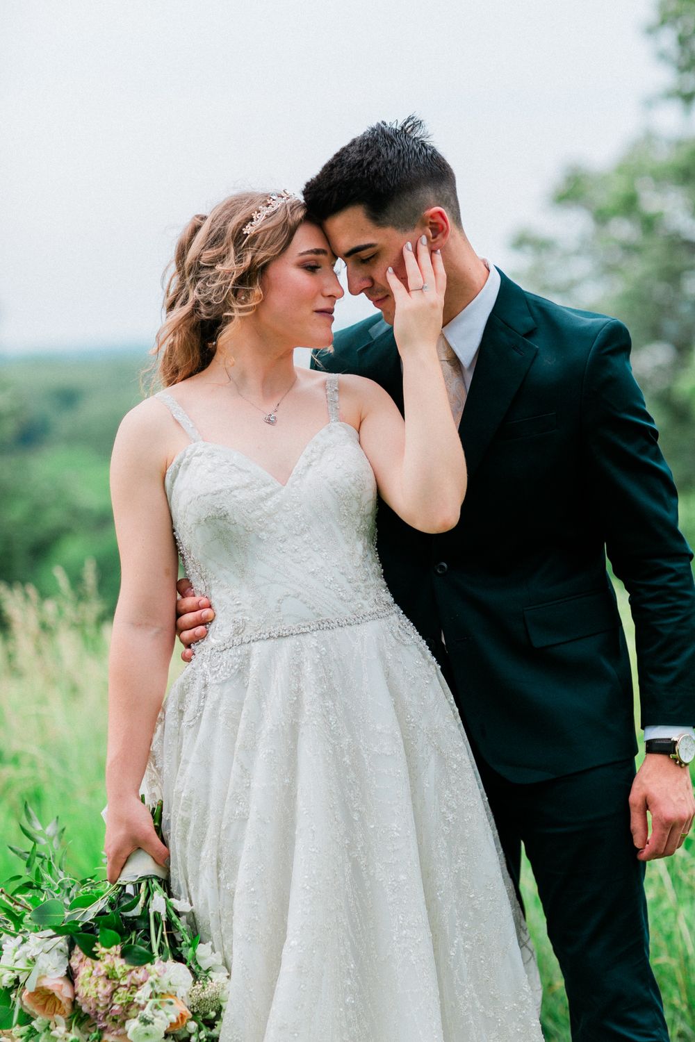 Romantic bride and groom embrace in an intimate outdoor moment against a scenic green background.