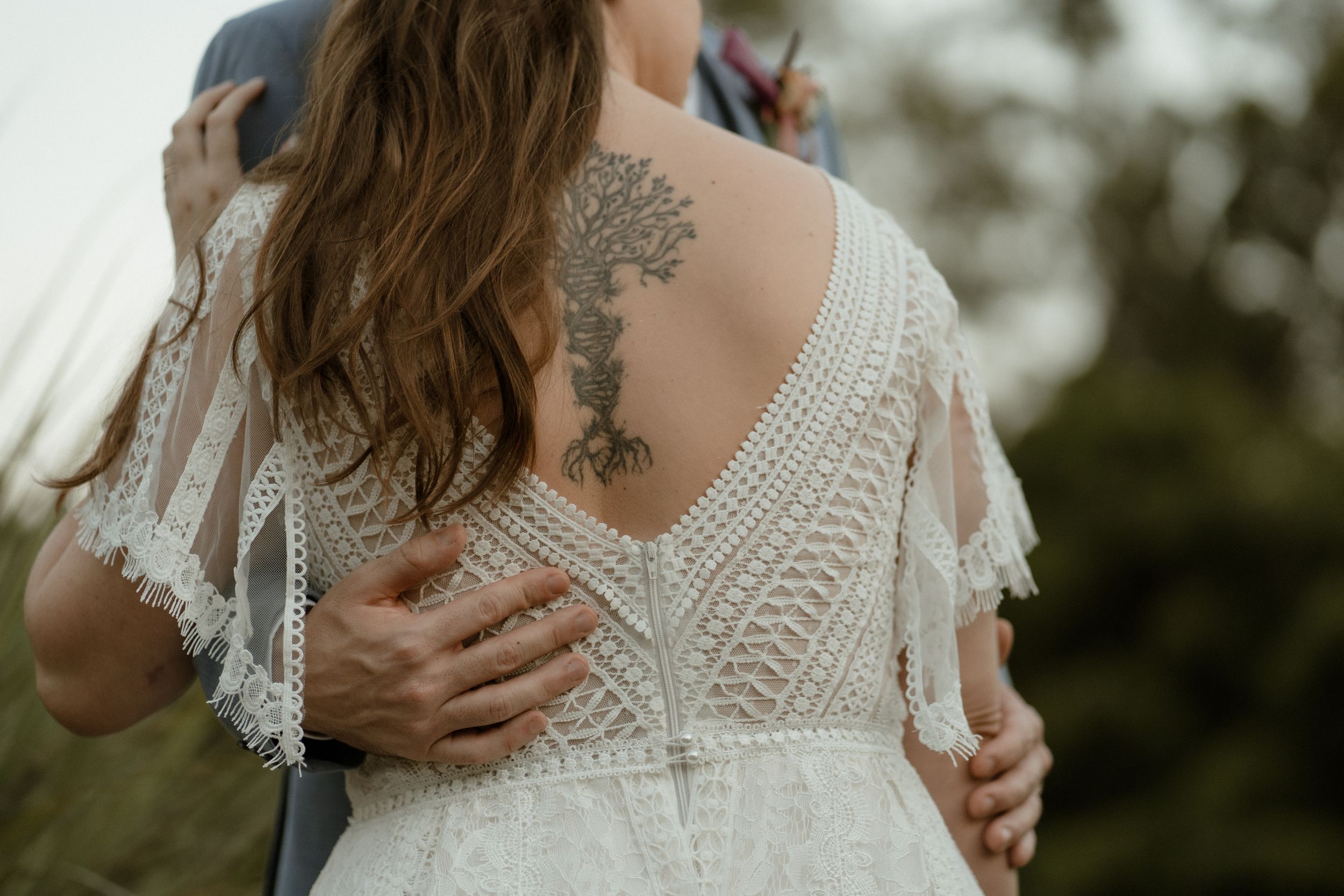 Intricate lace detail and floral tattoo visible on back of white wedding dress.