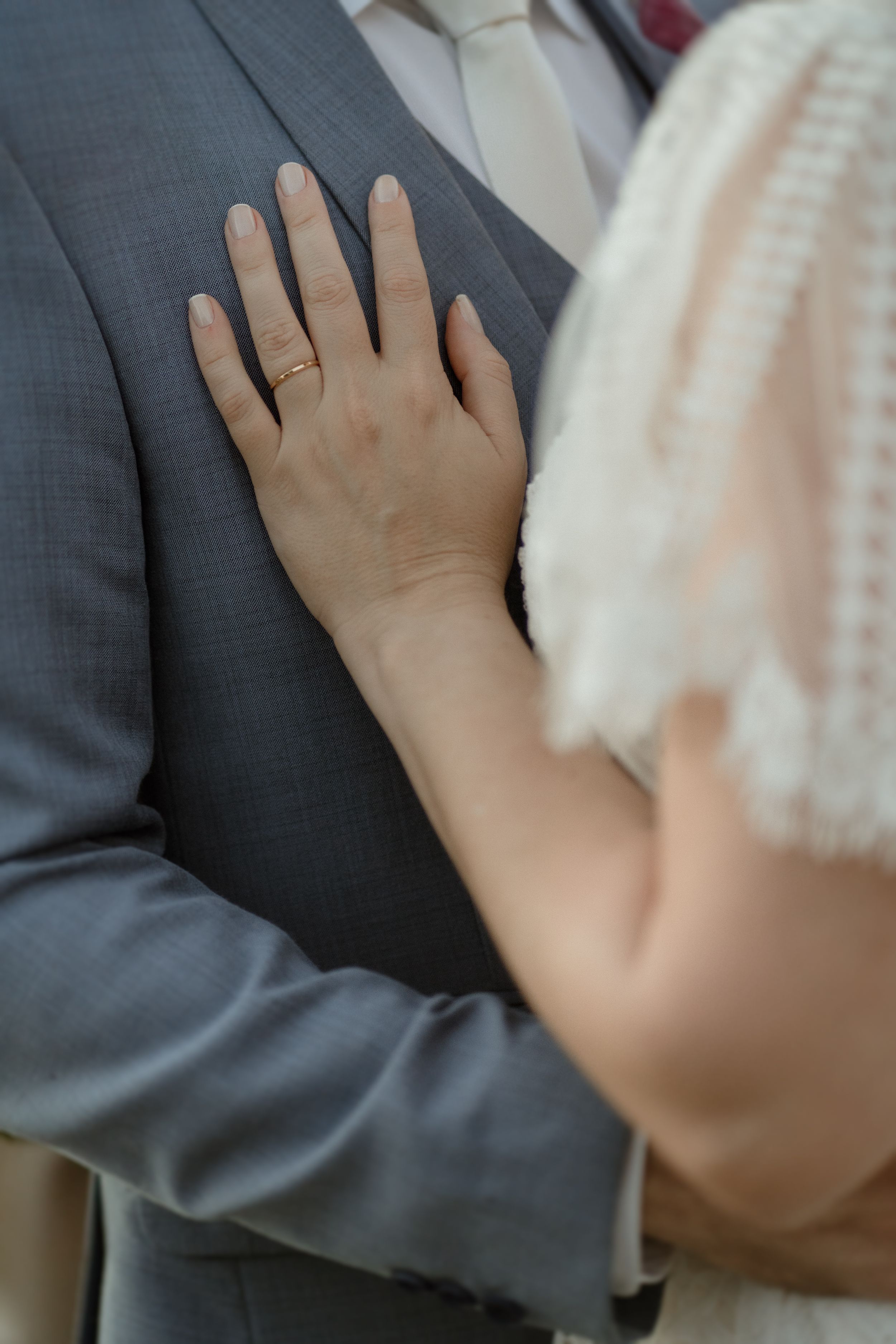 Close up of hands with wedding rings against a gray suit jacket.