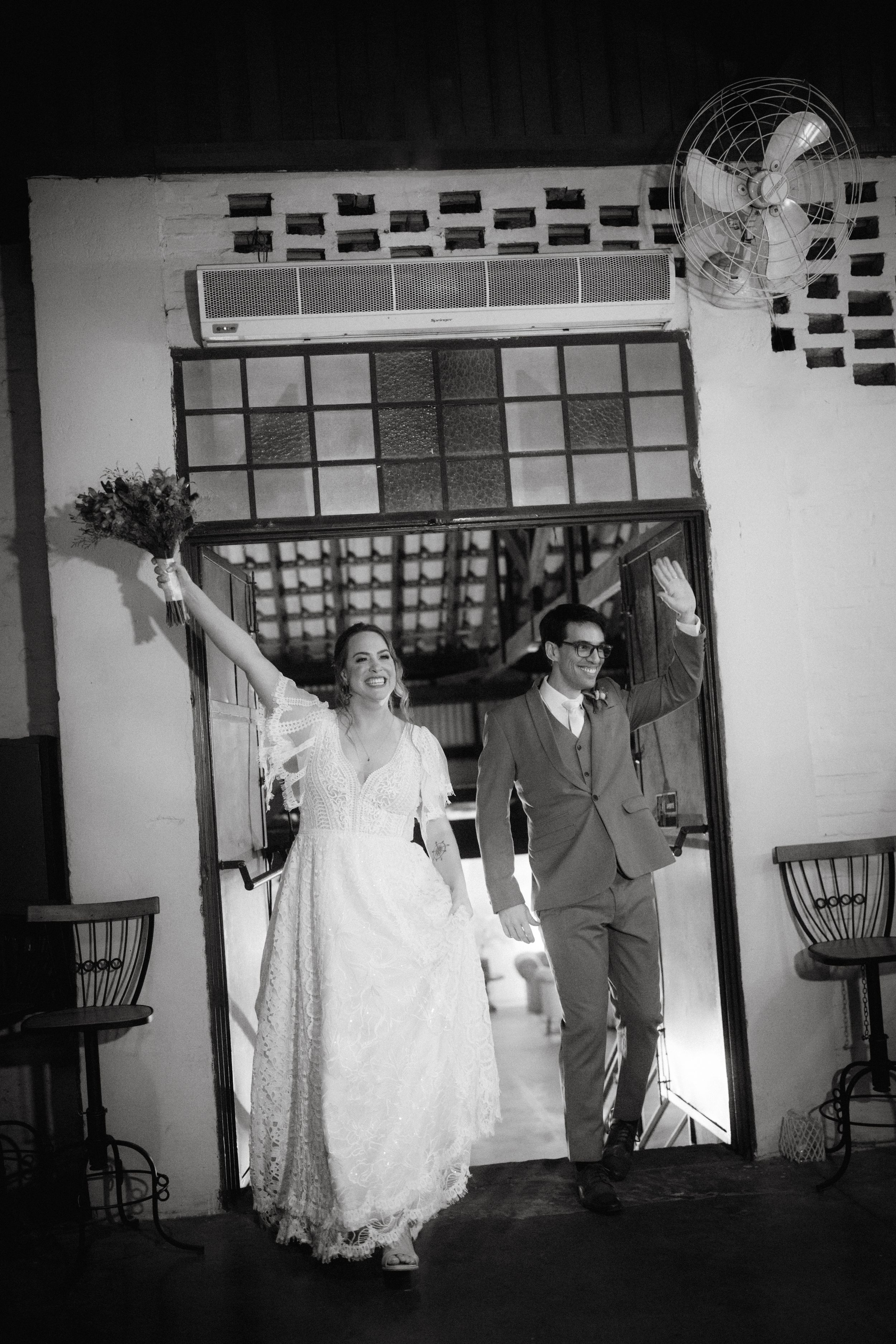 Black and white photo of wedding couple exiting through decorative doorway with raised bouquet.