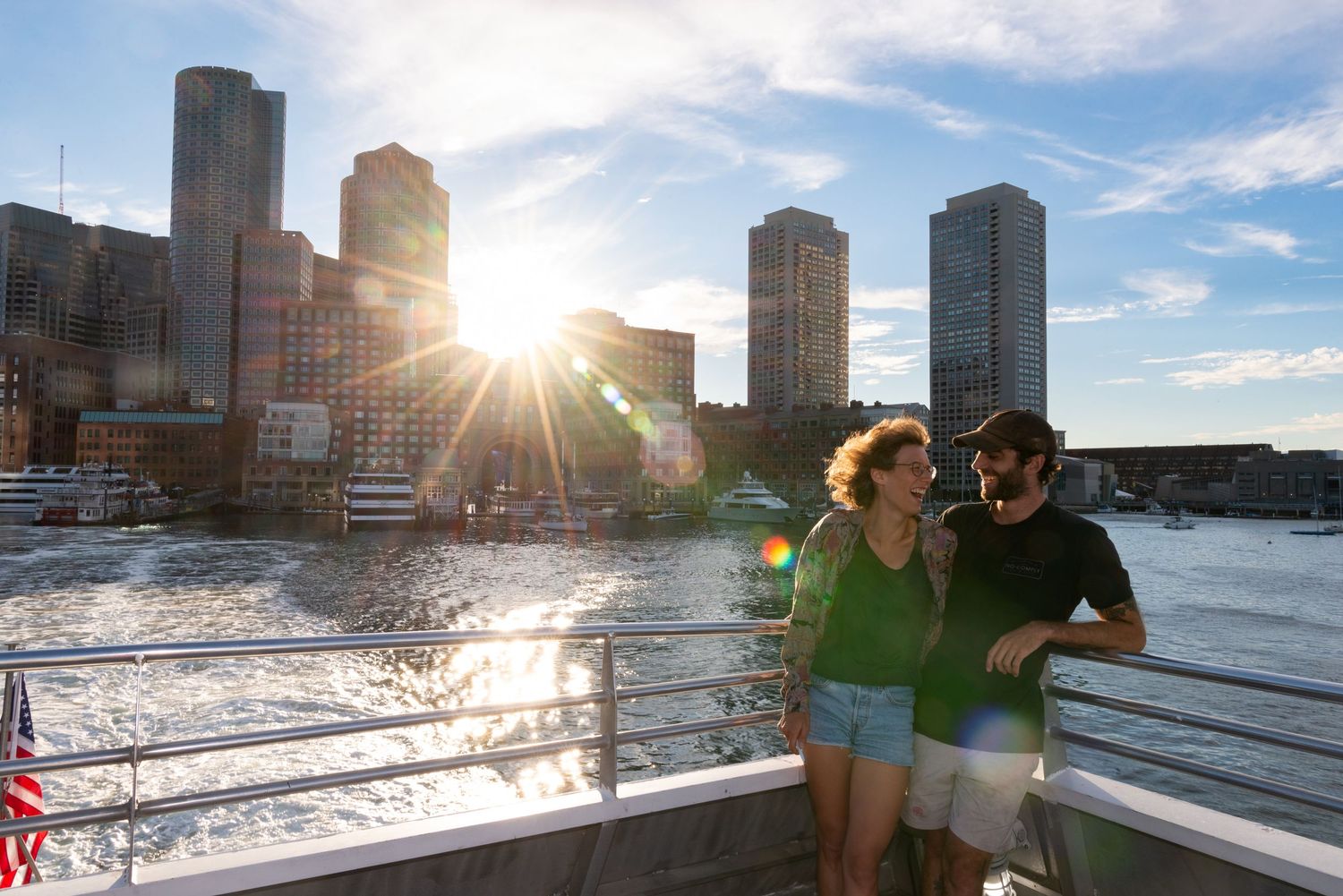 Professional photography on vacation in Boston, Massachusetts. Two tourists on a boat at sunset with the Boston skyline in Boston Harbor.