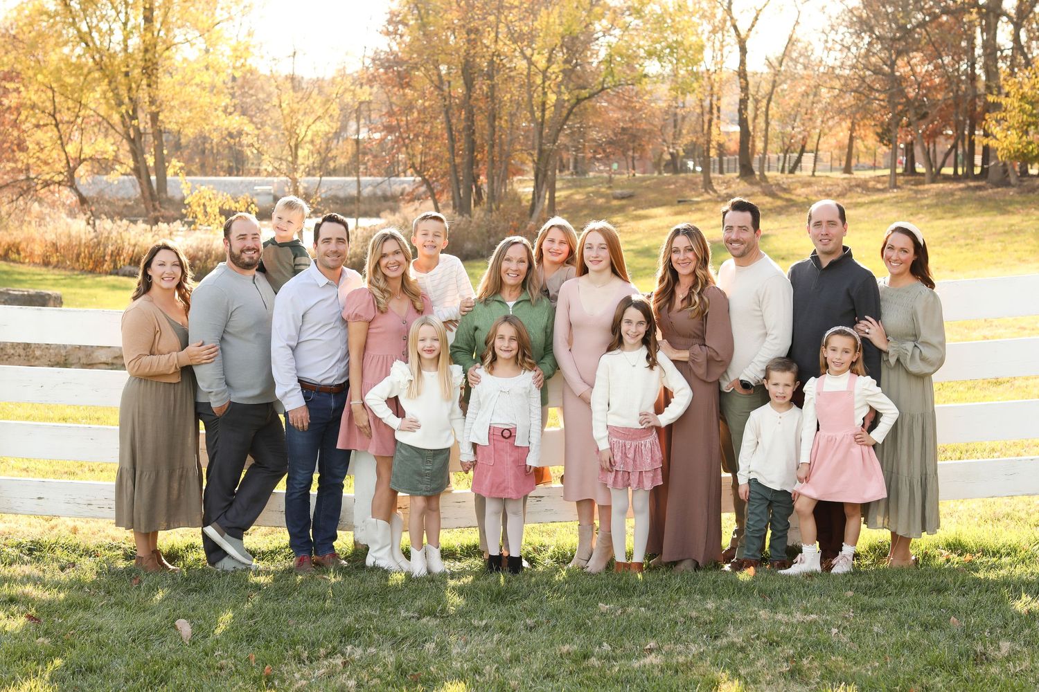 Extended family portrait session at golden hour with rustic fence and fall foliage.