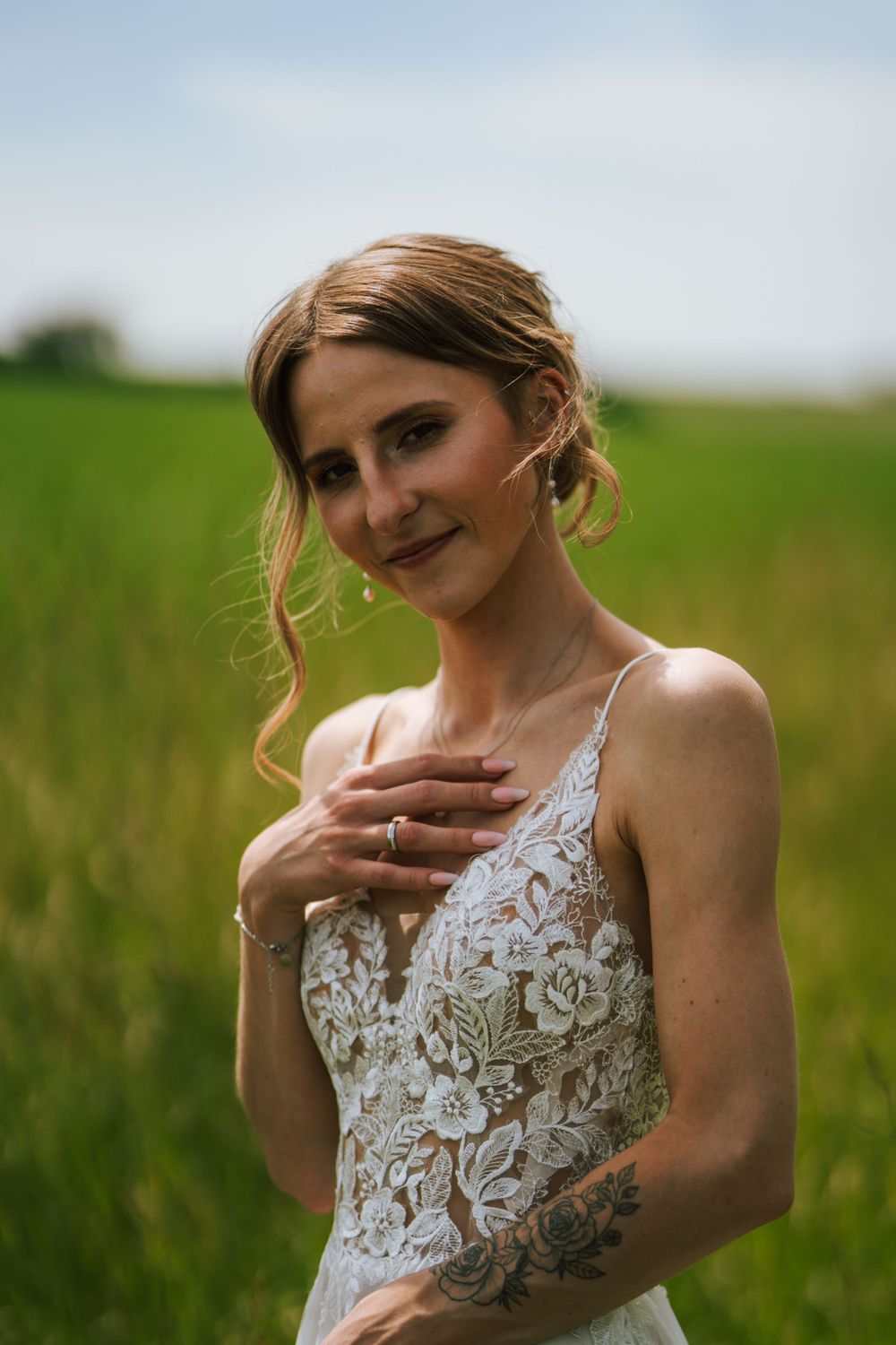 Bride in lace dress poses expressively in sunny field.
