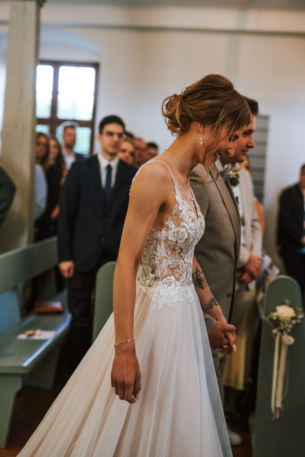 A bride in a flowing lace dress walks down the aisle during a wedding ceremony.