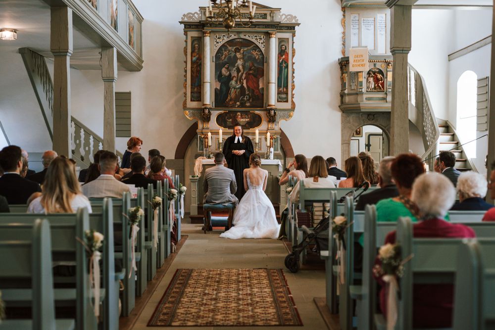 Wedding guests seated in wooden pews inside a traditional church with religious artwork.