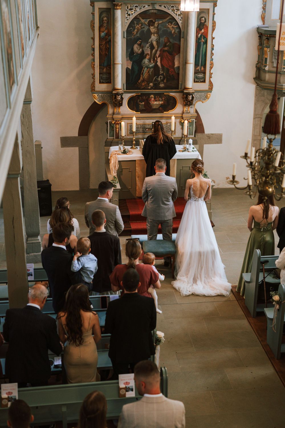 Wide view of a church wedding ceremony with guests seated in green pews.