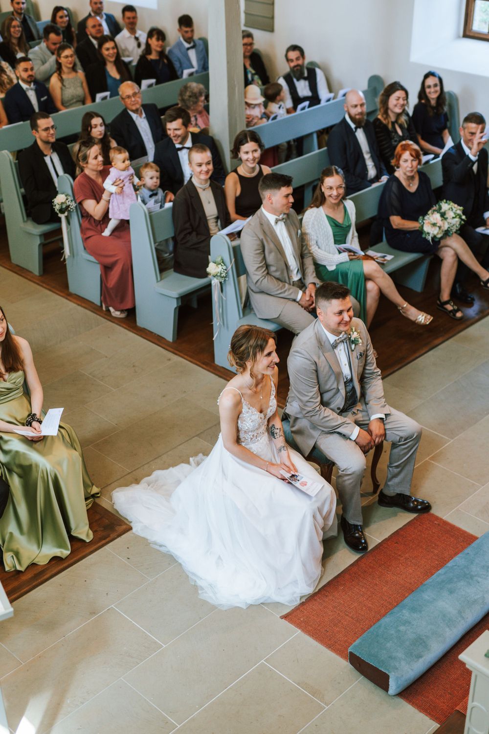 Wedding guests seated in church pews while couple sits in front during intimate ceremony.