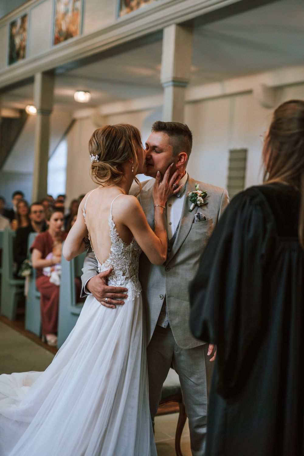Close-up detail of bride's lace dress and groom's gray suit during ceremony.