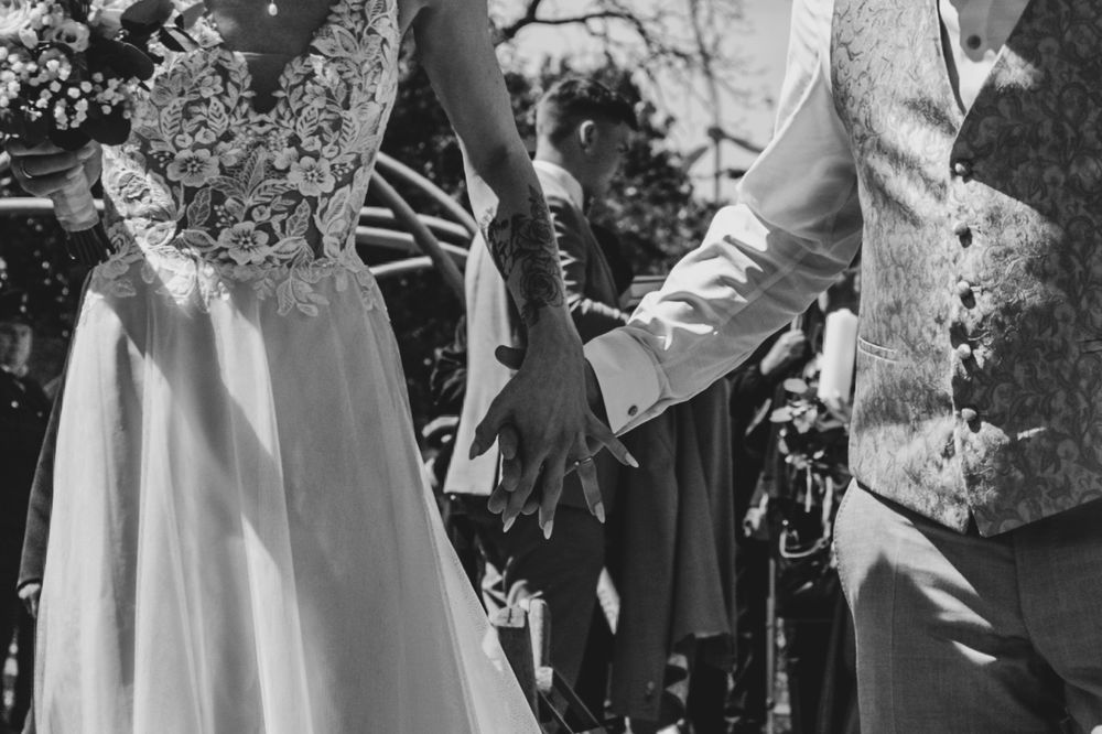 A black and white detail shot of a couple holding hands during their outdoor wedding ceremony.