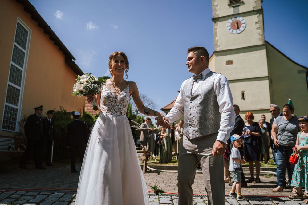 A joyful wedding celebration outside a church with guests in the background.