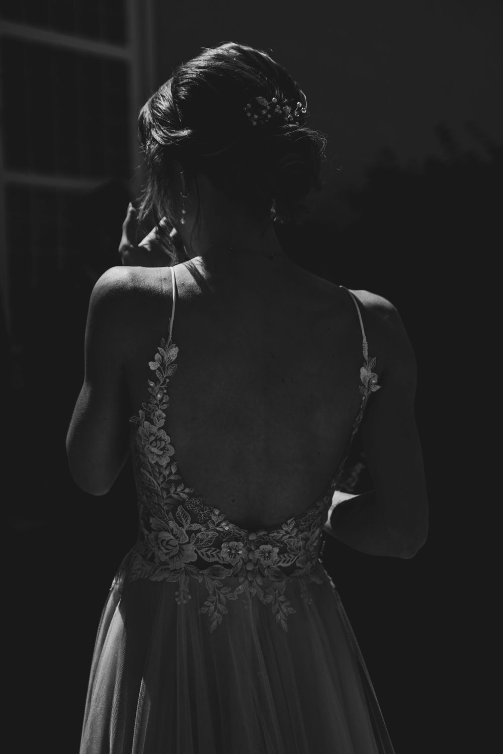 A dramatic black and white portrait showing the intricate lace back detail of a wedding dress.