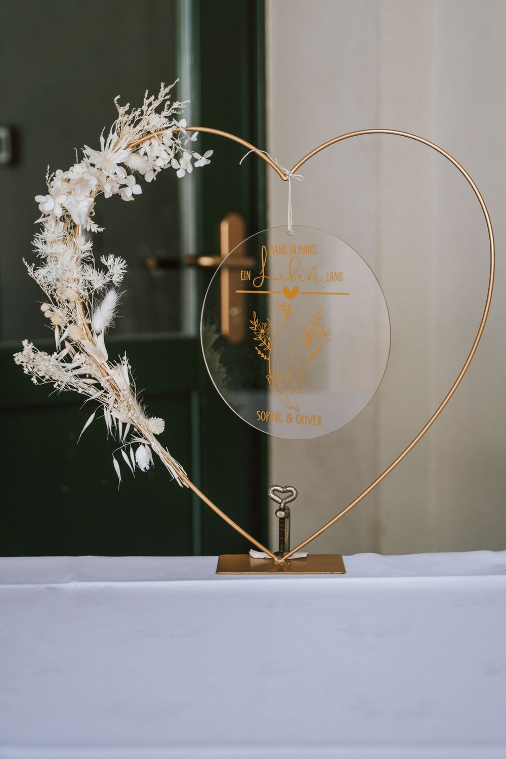 A decorative heart-shaped wedding sign holder with dried white flowers on display.