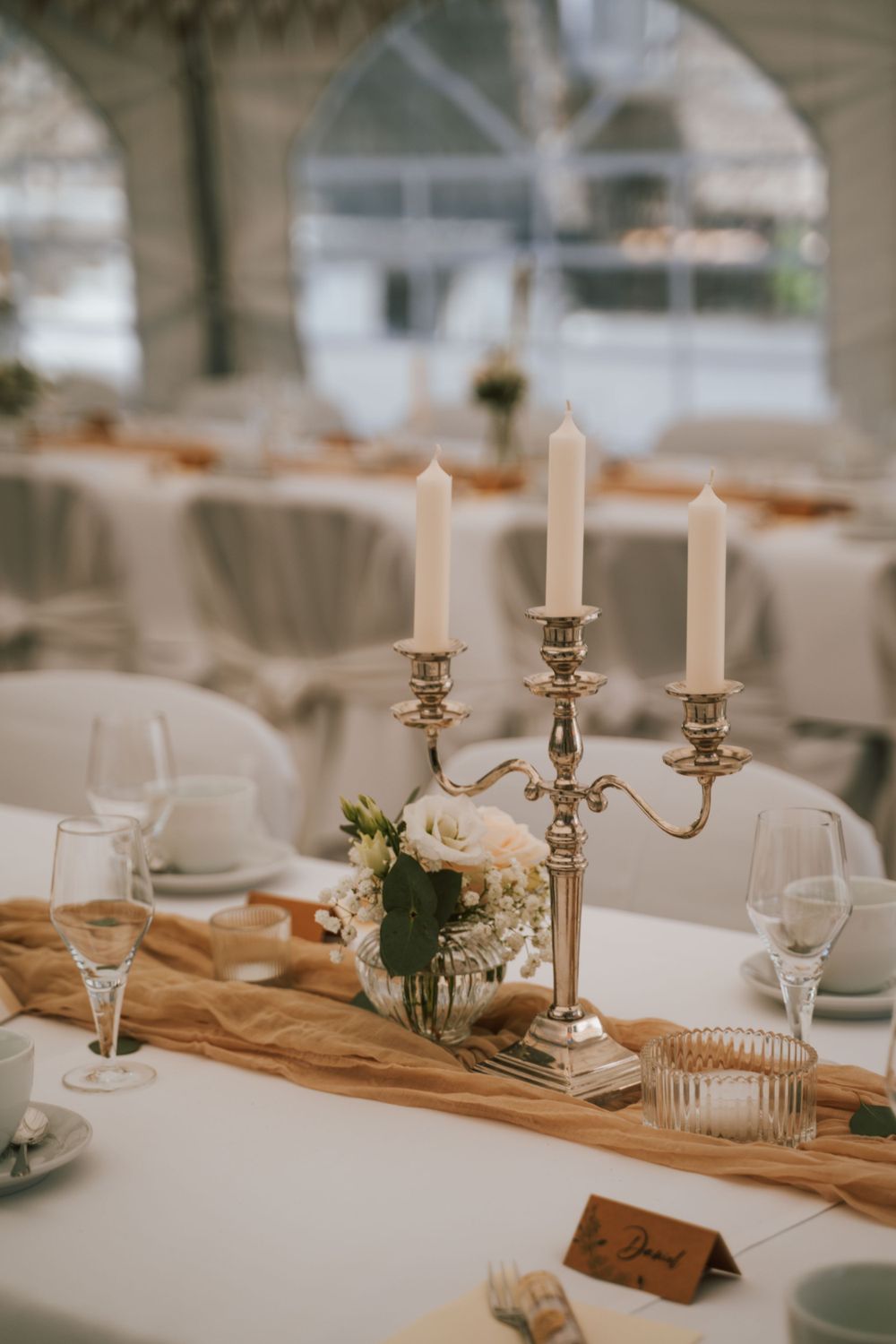 An elegant wedding table setting with silver candelabra, white flowers and champagne-colored runner.