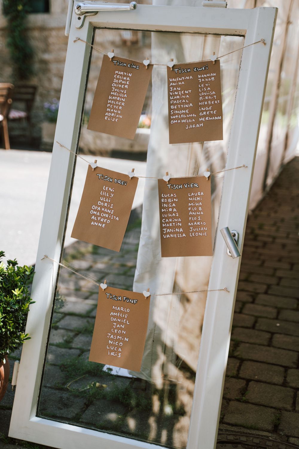 A vintage window frame displaying kraft paper seating charts for wedding guests.