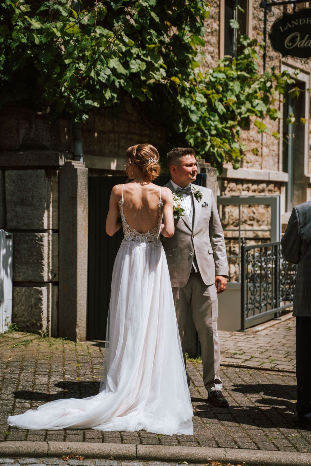 A wedding couple poses together on a cobblestone street with greenery and stone buildings in the background.