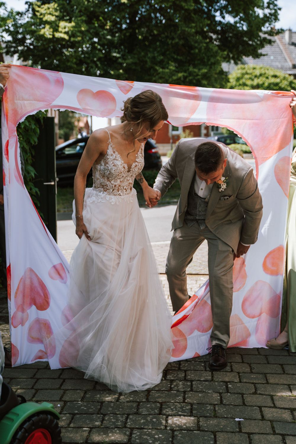 A couple poses playfully behind pink and white decorative banners at their wedding.