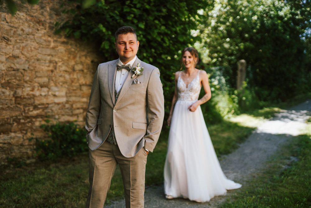 A wedding couple poses in a garden path with stone walls and lush greenery.