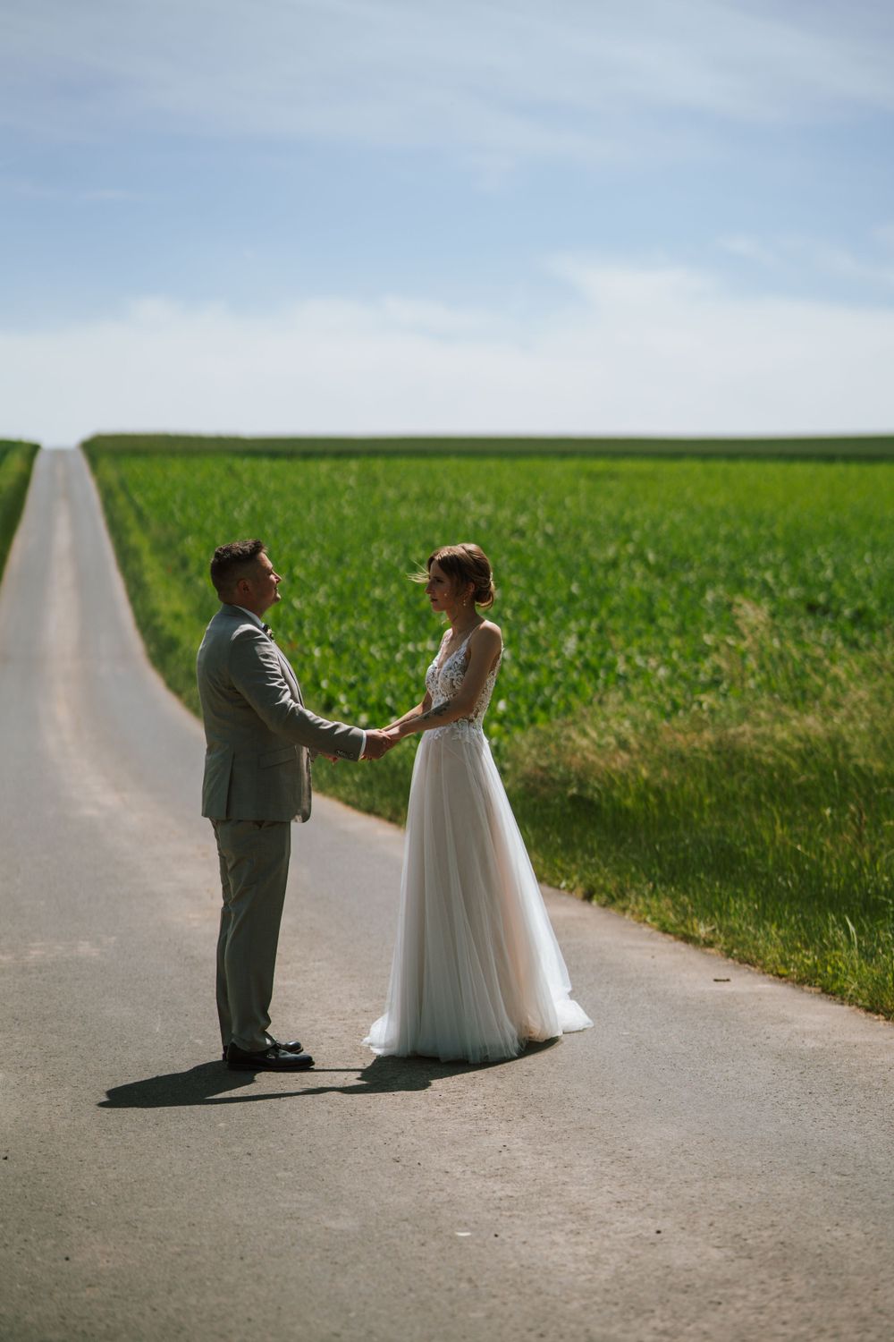 A romantic wedding moment captured on a long country road between green fields.