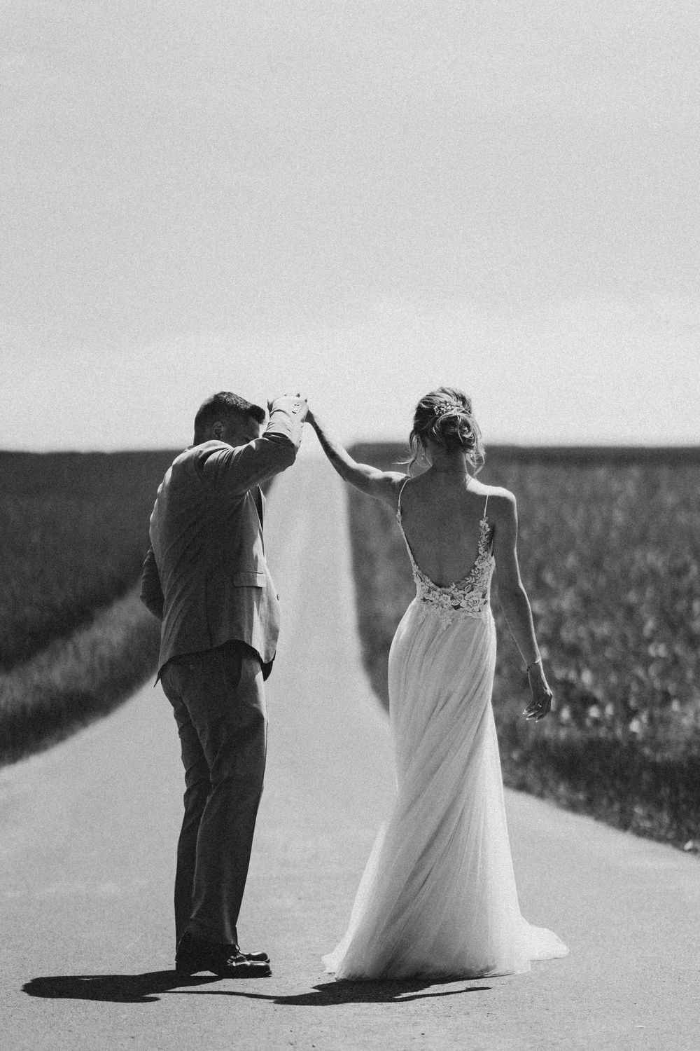 A black and white photo of newlyweds dancing on a countryside road.