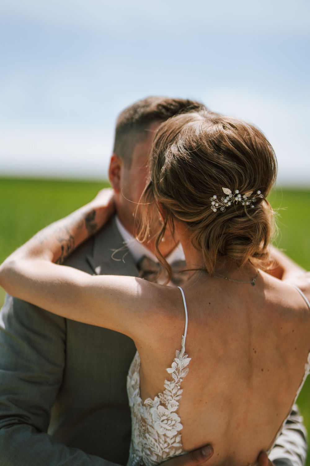 A close-up view of a bride's lace dress back detail and elegant updo hairstyle with crystal accessories.