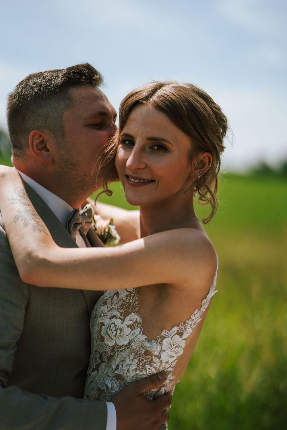 An intimate wedding portrait showing tender moments between newlyweds in a sunny field.