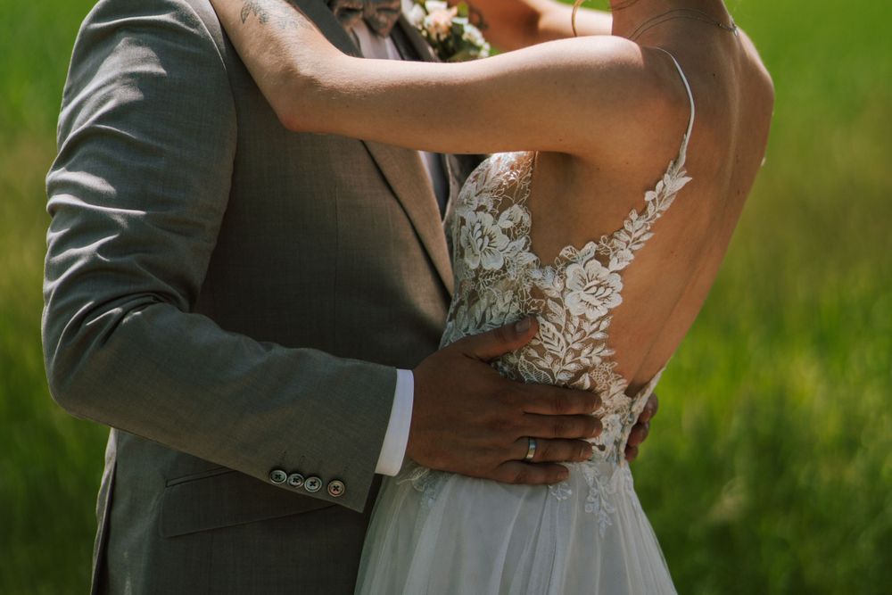 Detail shot of wedding couple embracing, showing intricate lace dress and gray suit.