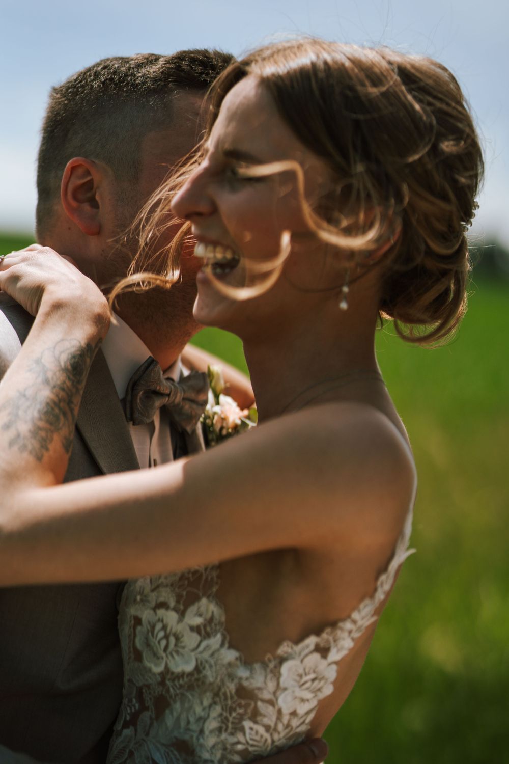 Joyful candid moment between newlyweds sharing laughter during outdoor wedding photos.
