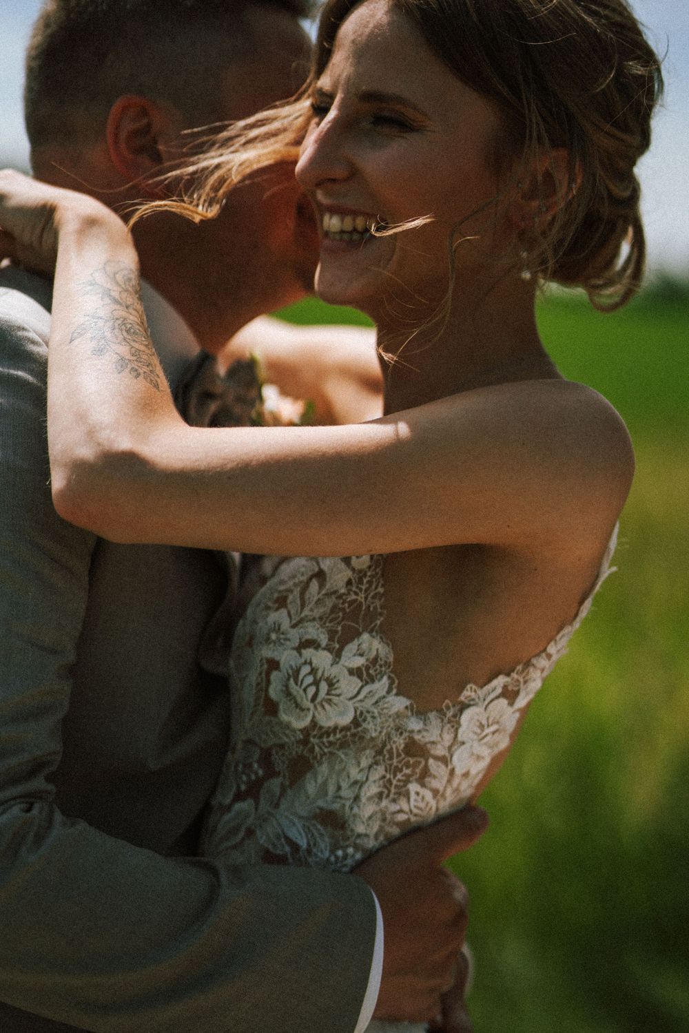 Sun-kissed portrait of bride in lace dress laughing during intimate wedding moment.