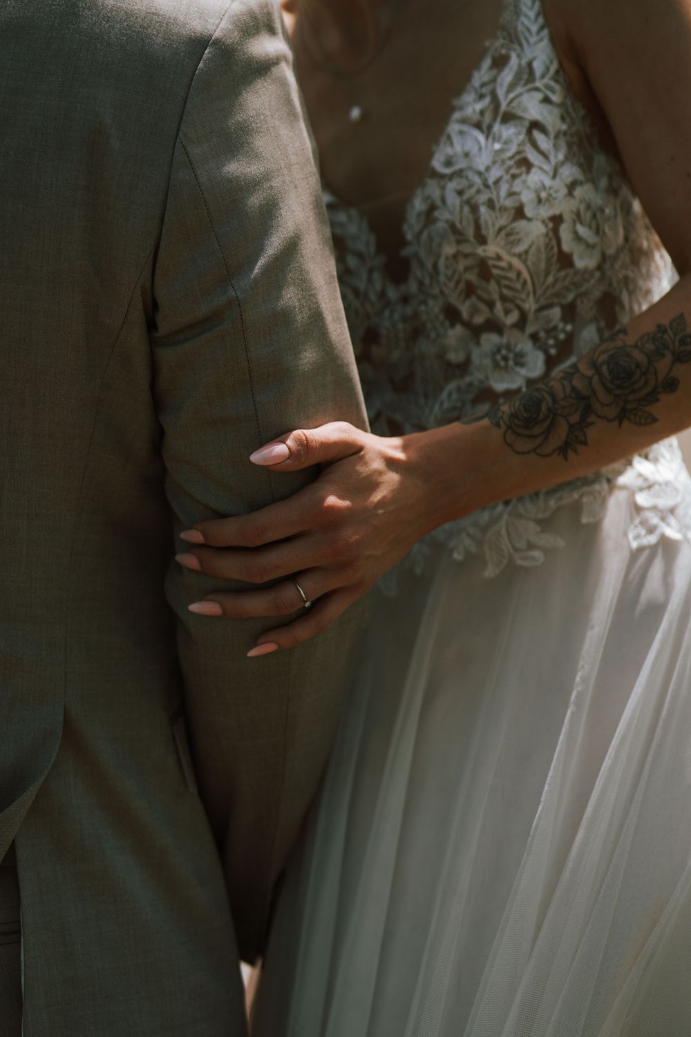 Close-up detail of a bride's hand with wedding ring resting on groom's grey suit.