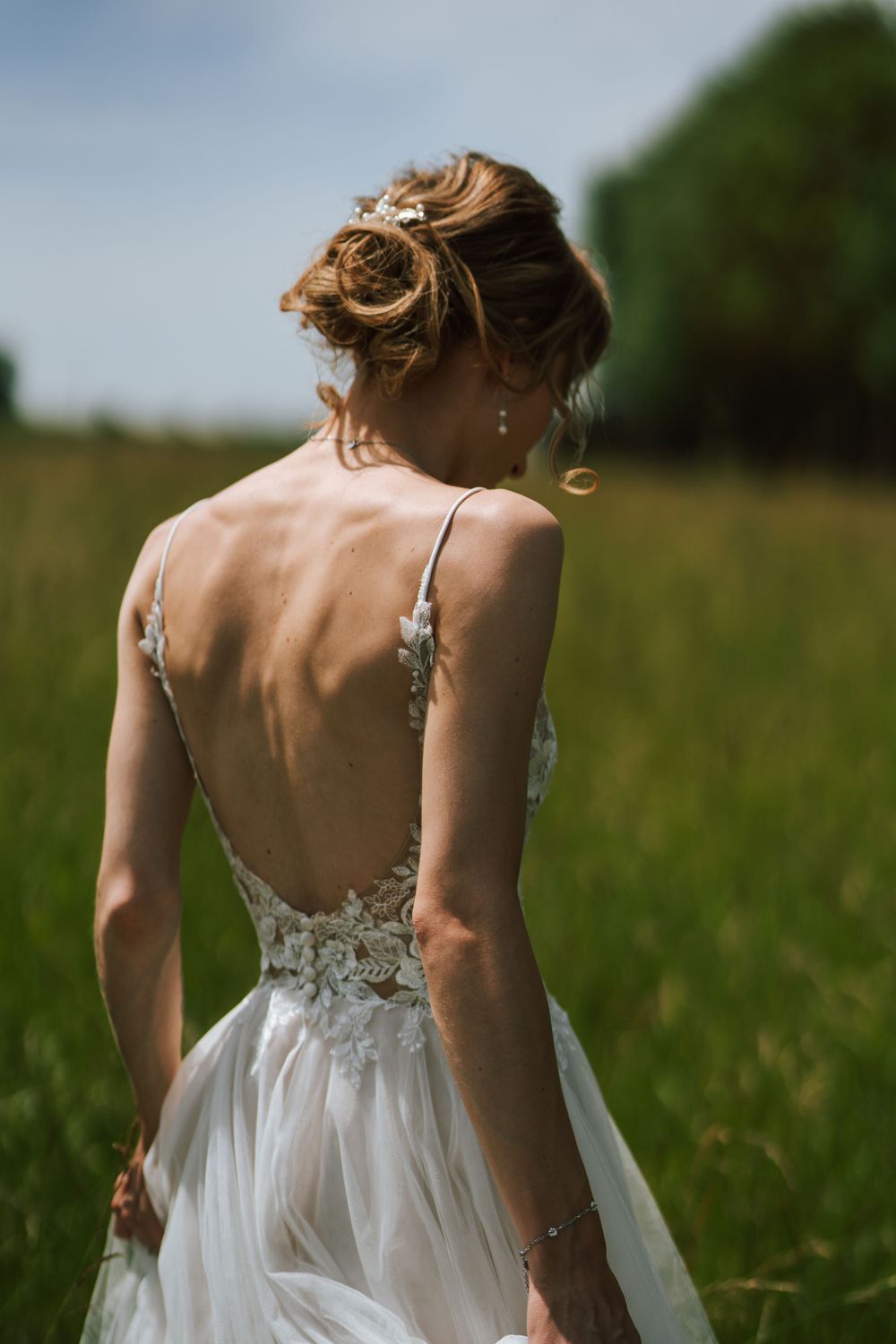 Back view of a bride's elegant updo hairstyle and lace detailed wedding dress in a field.