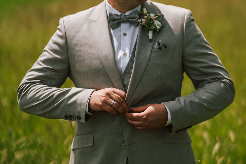 Close-up of groom in grey suit with boutonniere adjusting his bowtie.