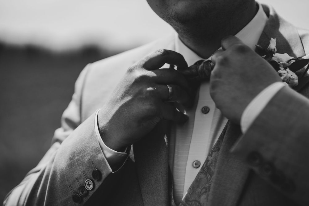 Black and white close-up of groom adjusting his bowtie before the ceremony.