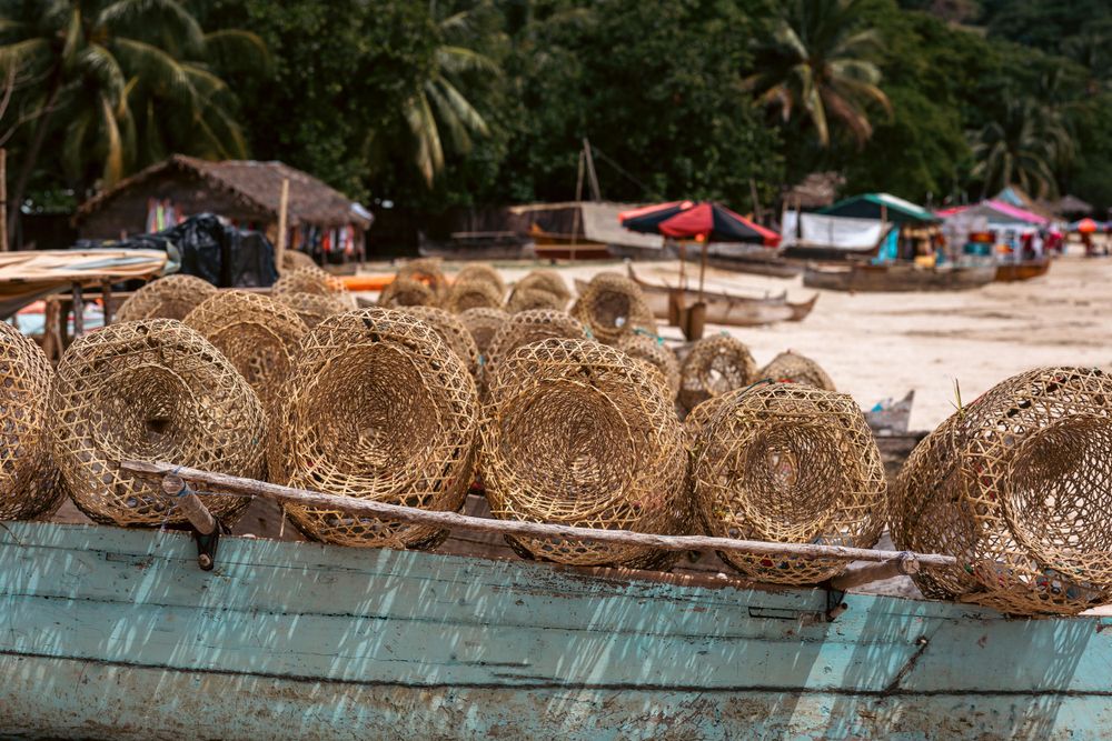 Traditional fishing traps and nets displayed on a wooden boat along a tropical beach shore.