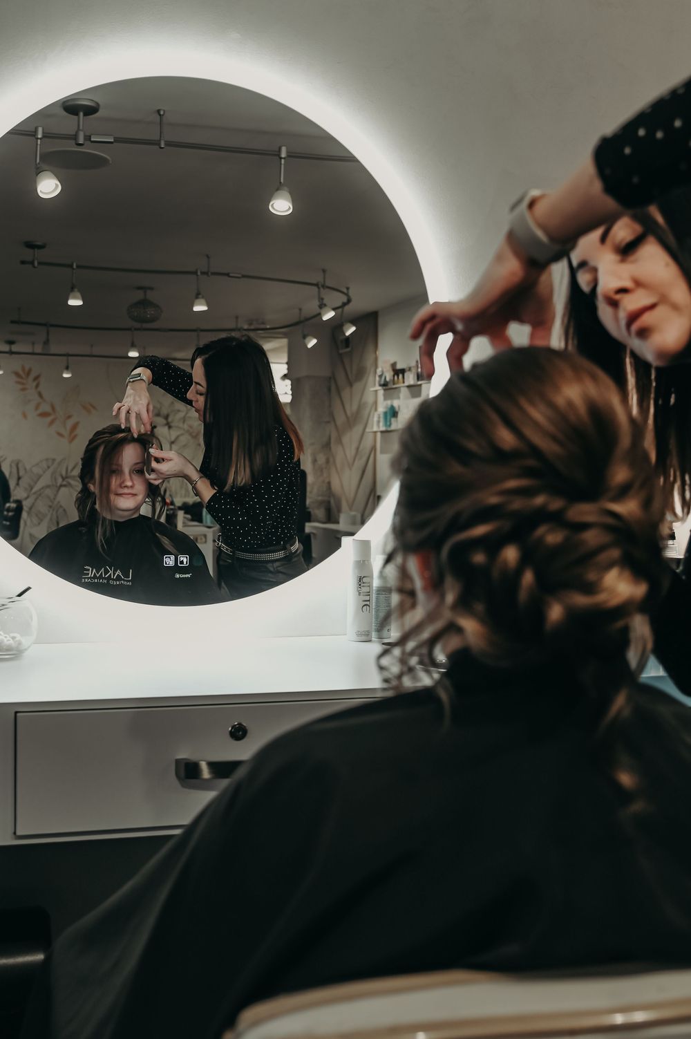 Hair styling session in progress at a modern salon with circular mirrors and warm lighting.