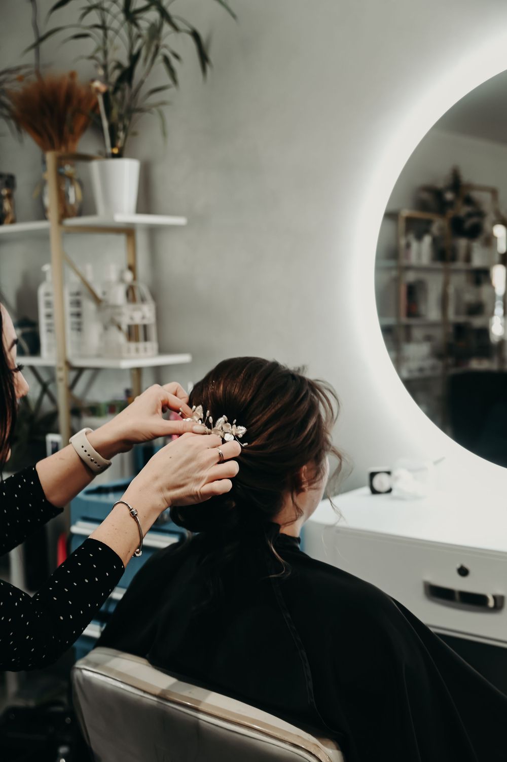 Close-up of hairstyling process with decorative plants visible in salon mirror reflection.