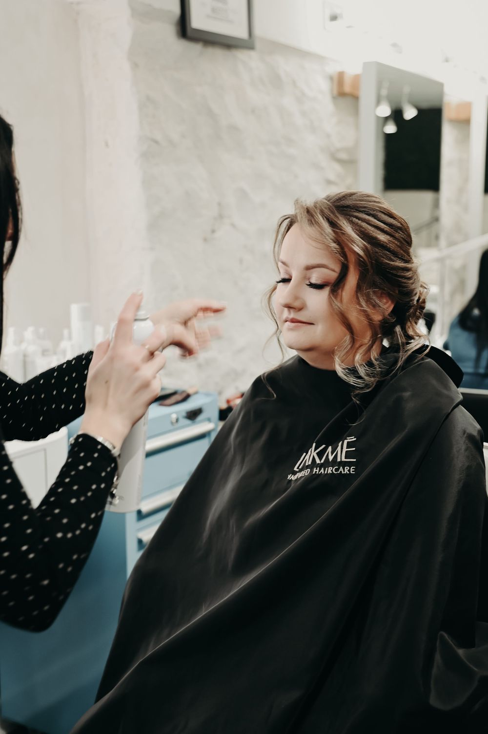 Client getting hair and makeup done while wearing a black salon cape.