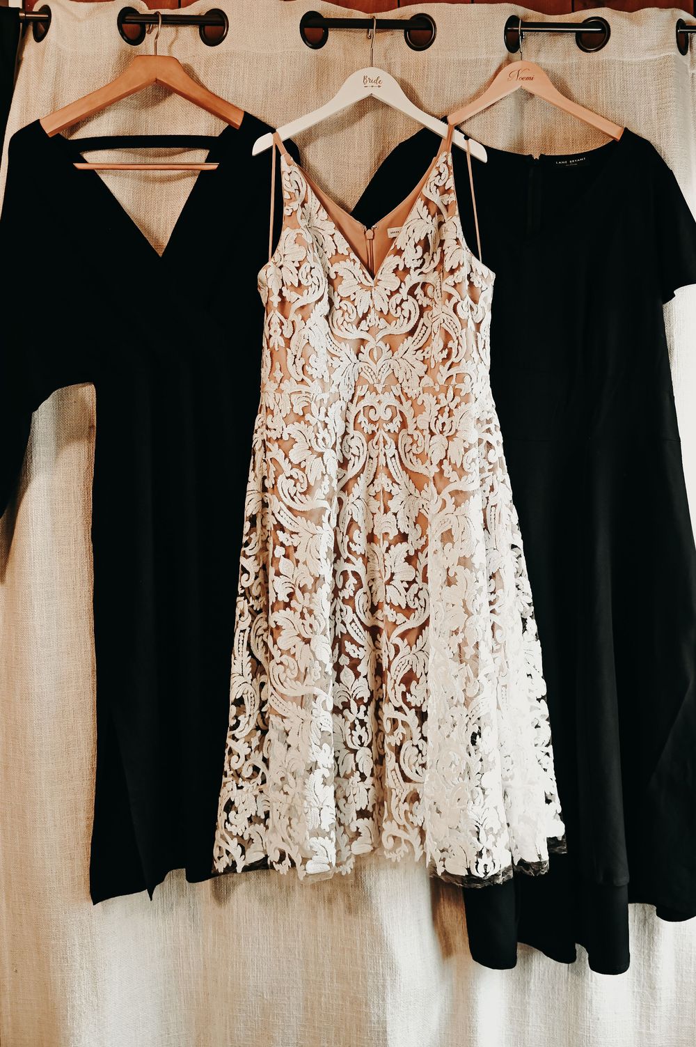 Row of black and white lace dresses hanging on wooden hangers against neutral wall.