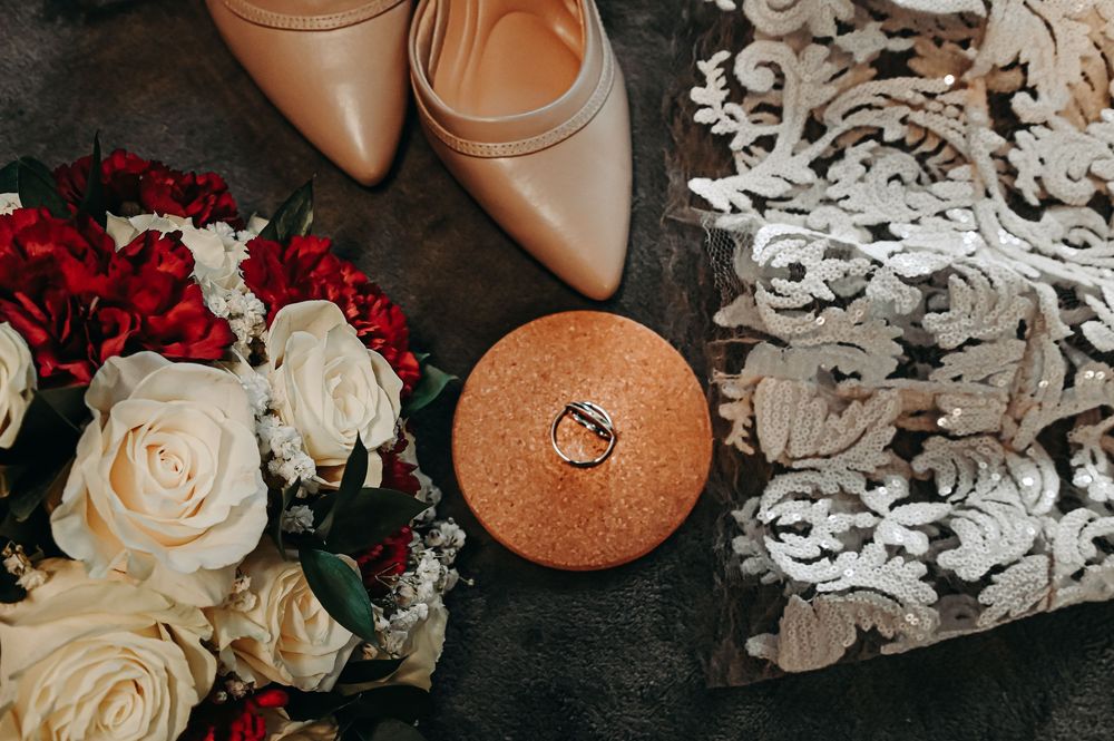 Wedding accessories flatlay with roses, lace details, and nude heels on dark surface.