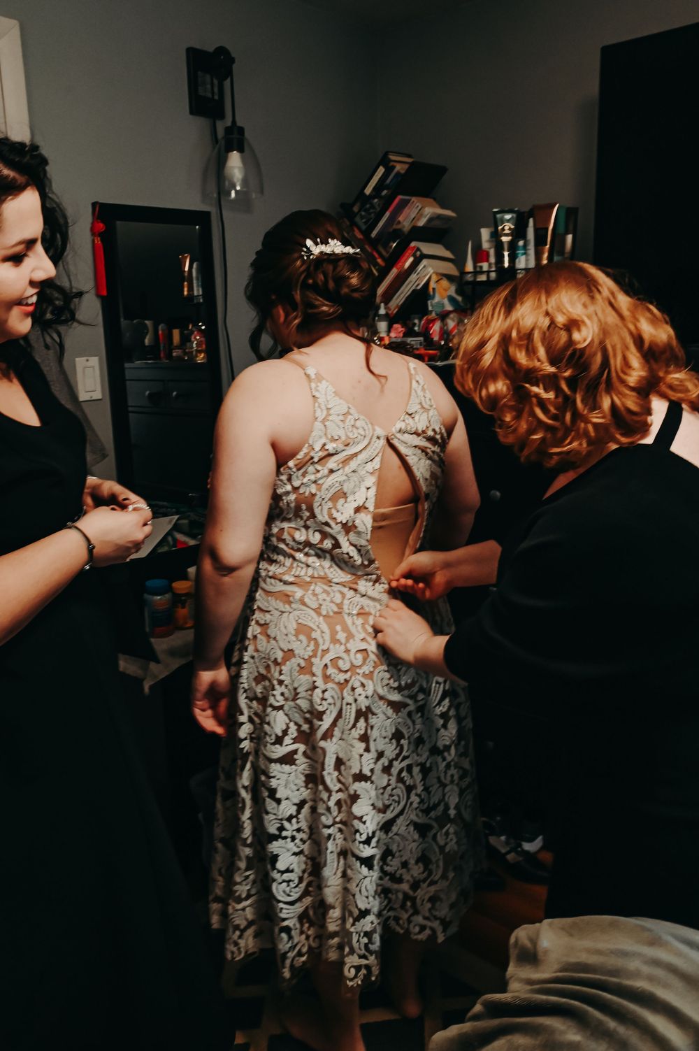 A lace dress being fitted and adjusted in a dimly lit dressing room.