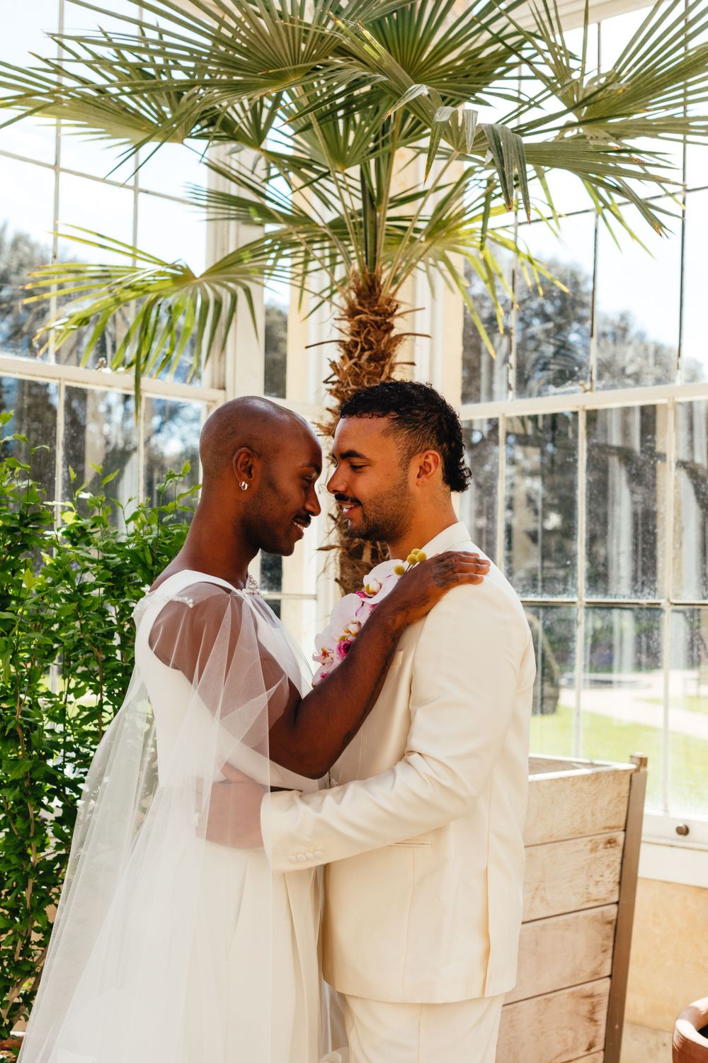 Couple shares an intimate moment under tropical foliage in elegant wedding attire.