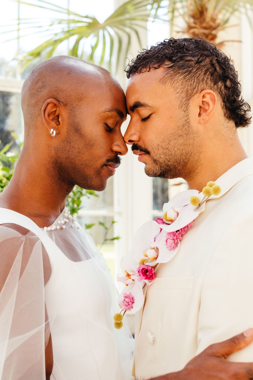Romantic wedding portrait showing two people in white sharing a tender moment beneath palm fronds.