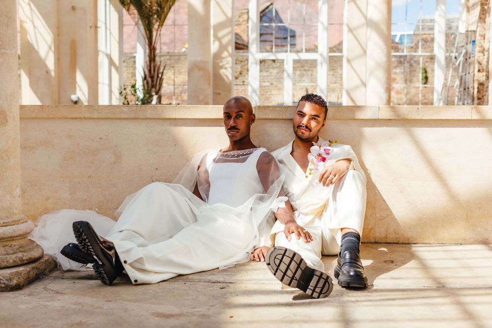 Wedding couple relaxes on conservatory floor in matching white outfits.