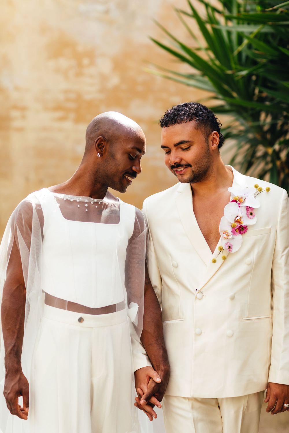 Intimate wedding photo of couple in white sharing a joyful moment against textured wall.